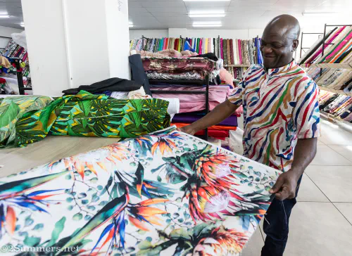 A salesman at Makotis unrolls a beautiful piece of fabric.